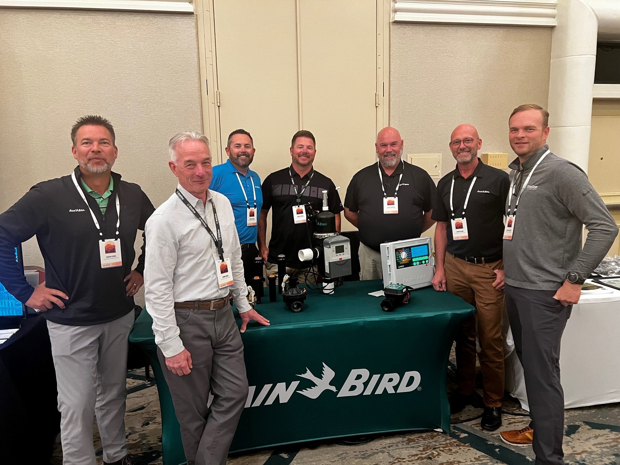 Rain Bird team stands by a product table with a green Rain Bird table cloth.
