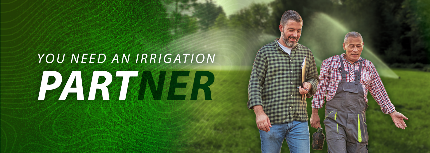 Landscape contractor walking alongside another man in a field with irrigation sprinklers shooting water in the background