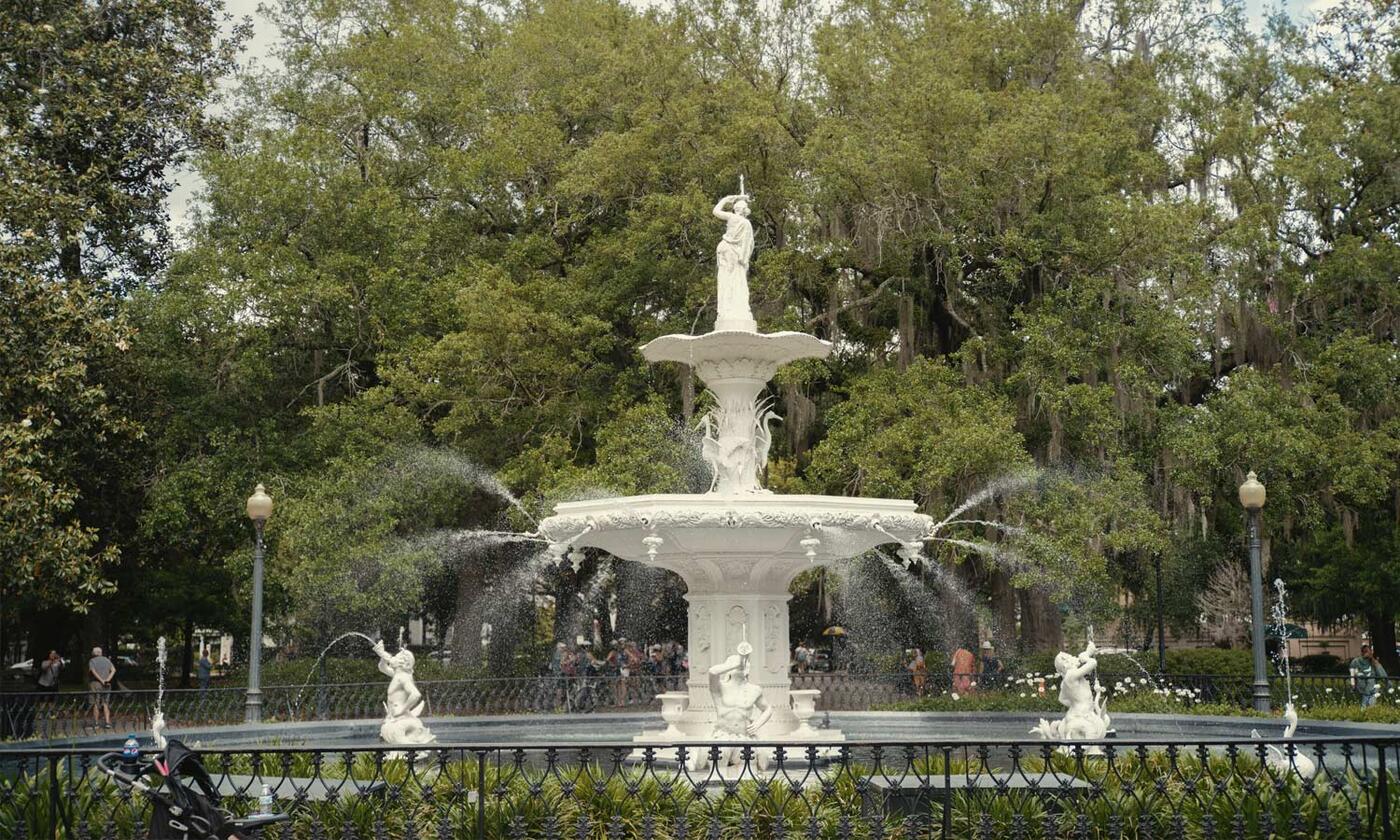 Water fountain shooting water in park with Candler live oak trees surrounding it